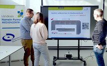 Drei Personen stehen vor einem Flat-Screen im Medienzentrum