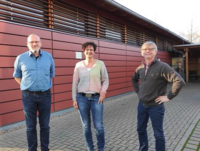 Foto: Drei Personen stehen vor einer Halle.png