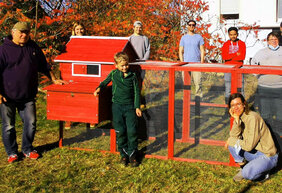 Menschen umringen einen selbst gebauten roten Hühnerstall