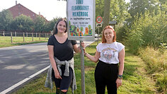 Zwei Frauen halten ein Schild mit der Aufschrift Flohmarkt
